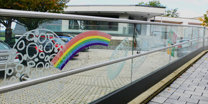 Zaun aus Glas vor den dem Gebäude mit einer Abbildung von einem Regenbogen 